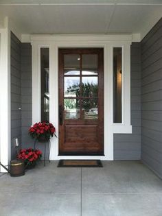 a front door with two red flowers on the side and one potted planter