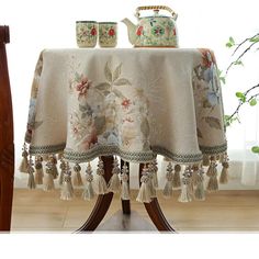 the table cloth has tassels on it and is next to a vase with flowers