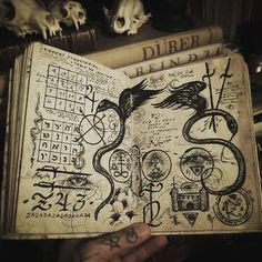 an open book with writing on it in front of skulls and other items that are sitting on top of a table