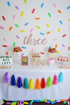 a table topped with lots of cake next to a wall covered in confetti