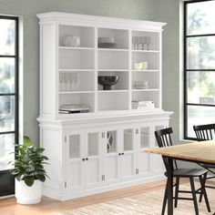 a dining room table with chairs and a china cabinet in front of two large windows