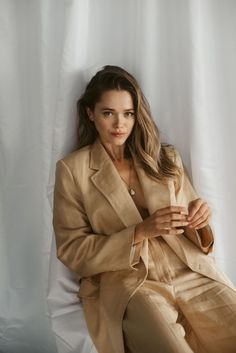 a woman sitting on top of a white chair wearing a tan suit and pearls necklace