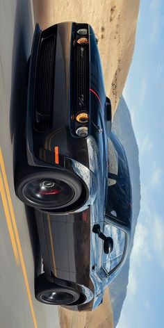 the rear end of a black sports car driving down a road next to a cliff