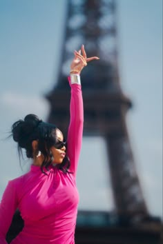 a woman in a pink dress standing next to the eiffel tower with her hand up