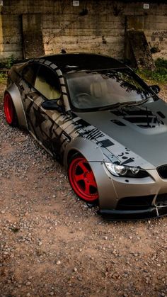 a silver car with red rims parked on gravel