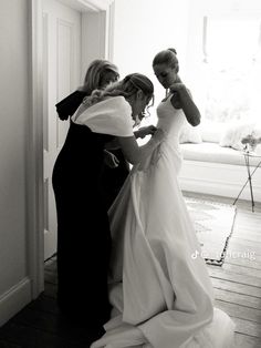 two women in dresses are helping another woman put on her wedding dress