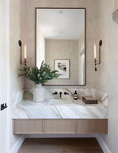 a bathroom vanity with marble counter top and large mirror above it, along with two candles on the wall