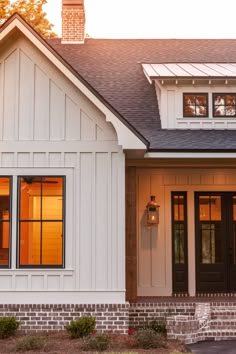 a white house with black doors and windows on the front porch is shown at sunset