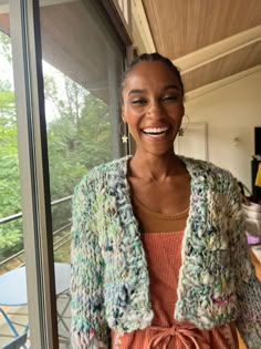 a woman standing in front of a window wearing a cardigan and smiling at the camera