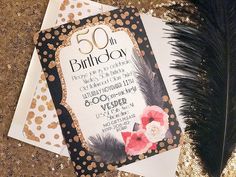 a 50th birthday card with a black feather and red flower on it next to a gold foiled envelope