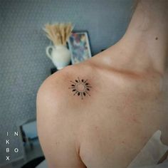 the back of a woman's shoulder with a small sun tattoo on it