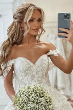 a woman in a wedding dress taking a selfie with her cell phone while holding a bouquet of baby's breath