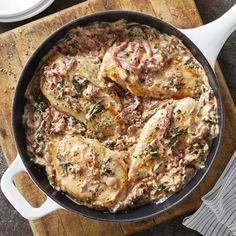 a pan filled with meat and sauce on top of a wooden cutting board next to utensils