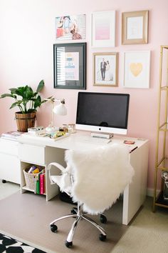 a white desk with a computer on top of it in front of a pink wall