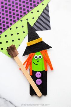 a paper witch holding a broom on top of a white table with black and green polka dots