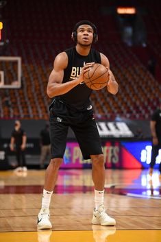 a man holding a basketball while standing on top of a basketball court in front of an arena