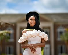 a woman wearing a graduation cap and gown posing in front of a building with her hands on her hips