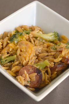 a white square bowl filled with pasta and broccoli on top of a table