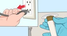 a person in blue gloves is plugging an electrical outlet with a white wall plate