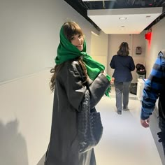 two people are walking down the hallway in an office building, one is wearing a green scarf