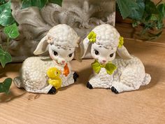 two ceramic sheep figurines sitting next to each other on a wooden table with ivy