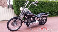 a black motorcycle parked on top of a brick road next to a fence and bushes