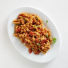 a white plate topped with pasta covered in sauce and basil leafy garnish