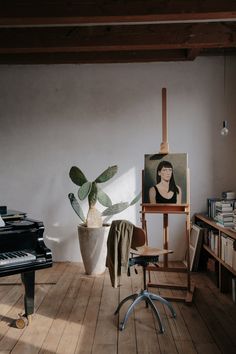 an easel with a painting on it next to a potted plant and a black piano