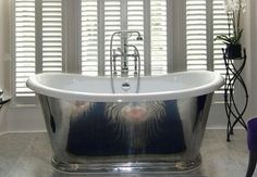 a bath tub sitting next to a window with shutters on the windowsill and a rug in front of it