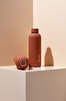 a brown bottle sitting on top of a white shelf next to a pink object in the corner