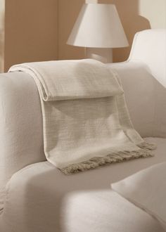 a white couch with a blanket on top of it next to a lamp in a room