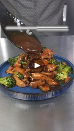 someone is pouring sauce on broccoli in a blue dish with the other side being drizzled over it