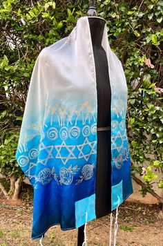 "A silk prayer shawl with matching bag for woman.  This one of a kind Jewish woman's prayer shawl (also called tallit in Hebrew) is made of silk crepe satin 12.5mm.  A painting of Jewish motifs on a white and blue prayer shawl wraps you with the divine spirit and holiness. The verse on the Atara :  פיה פתחה בחכמה ותורת חסד על לשונה Her mouth opened with wisdom and the law of kindness on her tongue.  One of the verses from the Eshet Hail prayer. Buy this tallit for the girl who celebrates her Bat Mitzvah.  Dimensions: 22\"/71\" (55 /180 cm) Materials: Silk crepe satin 12.5mm. Silk colors.  Care: Hand wash, iron on the rear side. Can be ordered with the following text on the ornament: \"ברוך אתה ה' אלוהינו מלך העולם אשר קדשנו במצוותיו וציוונו להתעטף בציצית\" -\"Baruch Atah Adonai Elokeinu Me Baruch Atah Adonai, Divine Spirit, Crochet Prayer Shawls, Painted Stripes, Jewish Women, Prayer Shawl, Sewing Workshop, Jewish Gifts, Star Of David