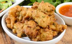 some fried food is in a white bowl on a wooden table with sauces and lettuce