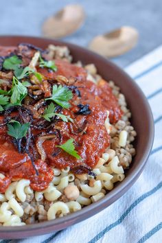 a bowl filled with pasta and sauce on top of a striped table cloth next to nuts