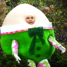 a person in a costume standing next to some bushes and trees with an egg on it's back