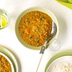 there is a bowl of soup on the table next to two plates with rice and limes