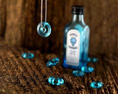 a bottle with a chain hanging from it next to some blue glass beads on a wooden surface