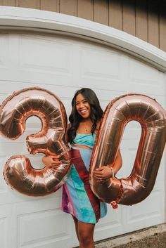 a woman standing in front of a garage holding two large balloons that spell out the number 30