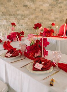 the table is set with red and pink flowers in vases, candles and napkins