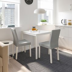 a white table with two chairs and a clock on the wall above it in a kitchen