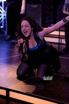 a woman is kneeling on the floor with her arms in the air as she sings