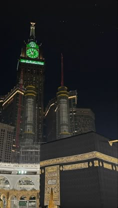 the clock tower is lit up at night in front of other buildings and skyscrapers