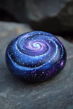 a purple and blue swirl painted rock sitting on top of a stone covered in stars