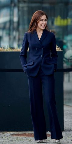 a woman in a blue suit standing on the sidewalk