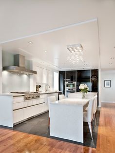 a modern kitchen with white furniture and wood flooring is seen in this image from the dining room