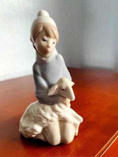 a figurine sitting on top of a wooden table holding a baby lamb in its arms