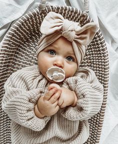 a baby with a pacifier in its mouth wearing a knitted sweater and headband