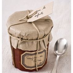 a jar of jam next to a spoon on a white tablecloth with a note in it