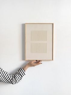 a woman is holding up a framed piece of artwork on the wall above her head